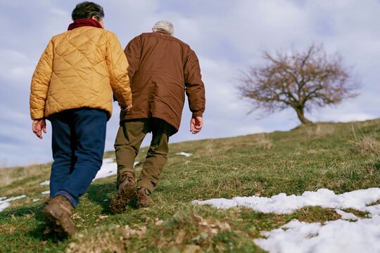 Couple walking hand in hand across a grassy hillside with lingering snow, a natural scene of companionship for retirement and wellness