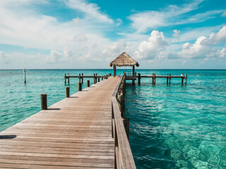 Obraz premium Wooden Pier Leading to a Thatched Hut Over Turquoise Tropical Waters