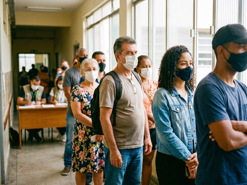 Diverse group of multiracial citizens wearing face masks standing in line in a corridor to vote or receive public services