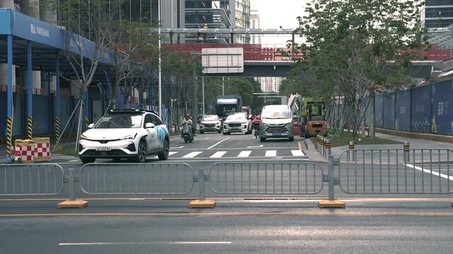 Midday traffic in Shenzhen, China. Many cars, buses, a driverless taxi, and scooters.