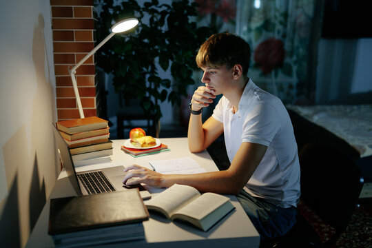 Focused teen student thinking while using a laptop for night homework.