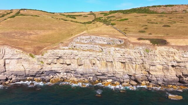 Aerial shot reversing away from the cliffs and caves with rock climbers on the Jurassic coast near Dancing Ledge in Dorset, UK