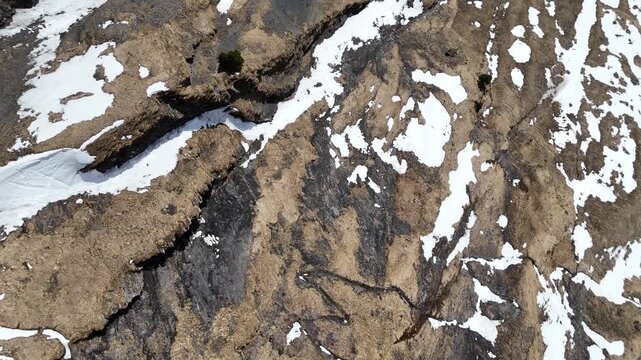 Aerial drone video looking down over a snowy alpine ridge in Switzerland, with patches of rock, snowfields, rugged terrain, and high mountain landscape.