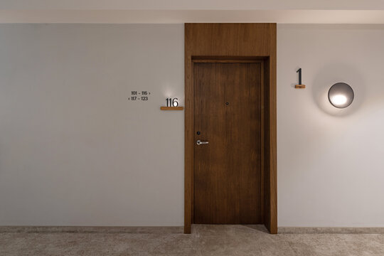Hotel room wooden entrance door with room number and wall lamp