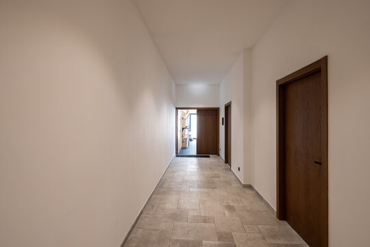 Empty modern hotel corridor with wooden doors and stone tile floor