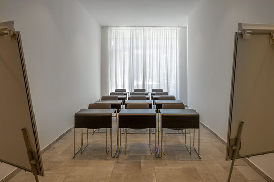 Modern empty conference room with rows of desks and white curtains