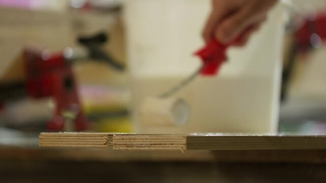 Worker applying glue to plywood with paint roller in woodworking shop