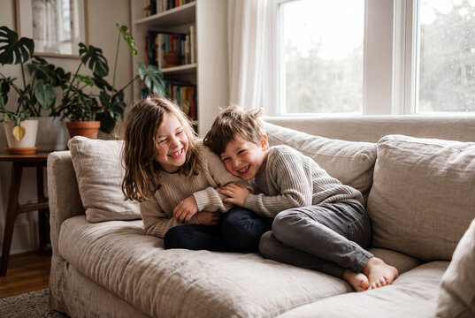 Happy siblings laughing together on living room couch