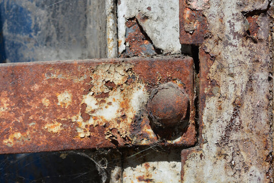 Close up shot of a heavily weathered and rusted iron hinge with peeling cream paint and cobwebs.