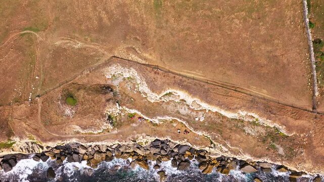 Aerial shot reversing away from the cliffs and caves with rock climbers on the Jurassic coast near Dancing Ledge in Dorset, UK