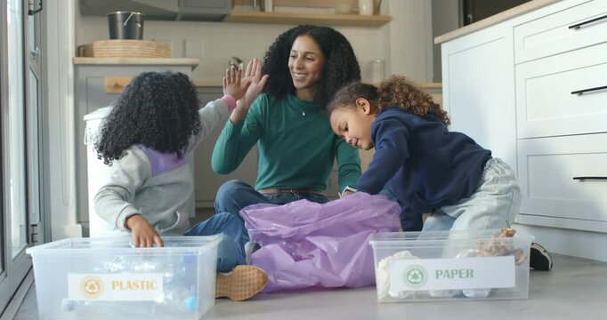African American mother guiding two children recycling, passing bottle, sorting into PLASTIC,PAPER
