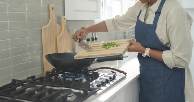 Cook is scraping chopped greens and garlic into heated wok on gas stove to start cooking