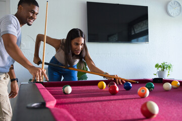 Fototapeta premium African American couple playing pool in game room, woman leaning, holding cue, balls on table
