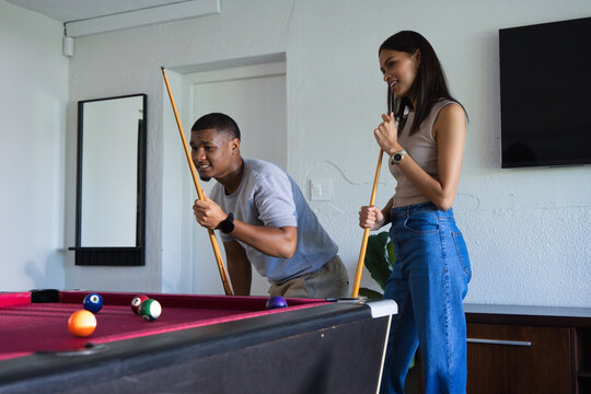 African American couple leaning, lining up pool shot at home on red felt table with balls