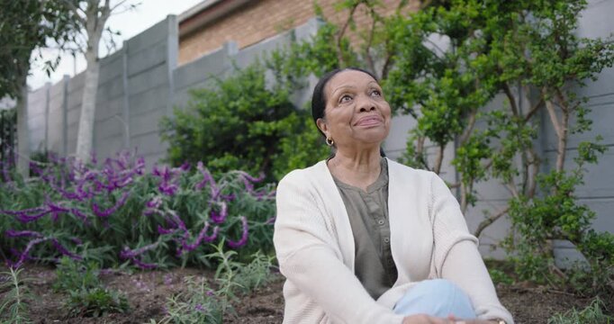 Camera zooming senior African American woman uncrossing legs smiling laughing in yard purple plants