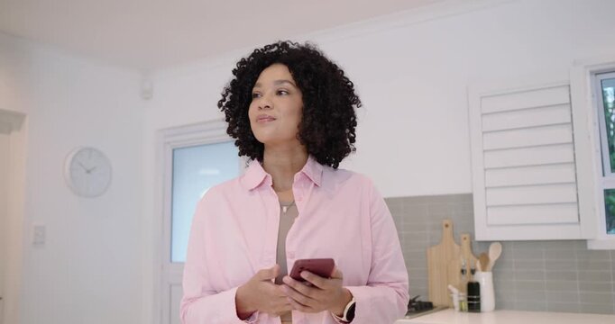 Adult woman in light pink shirt holding pink phone and tapping screen at kitchen counter smiling