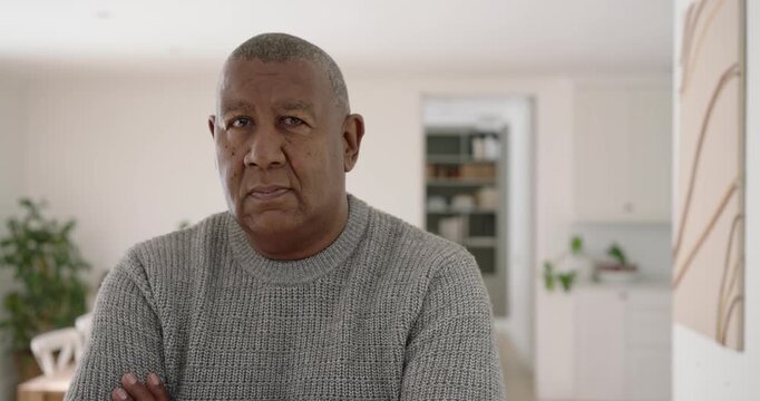 Mature African man arms crossed in kitchen, facing camera, smiling laughing in gray knit sweater