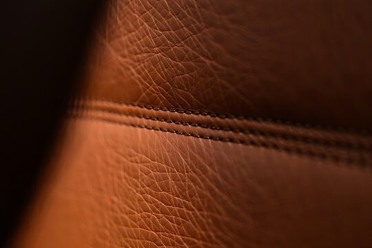 Close-up detail of rich brown leather texture with parallel stitching lines and natural grain