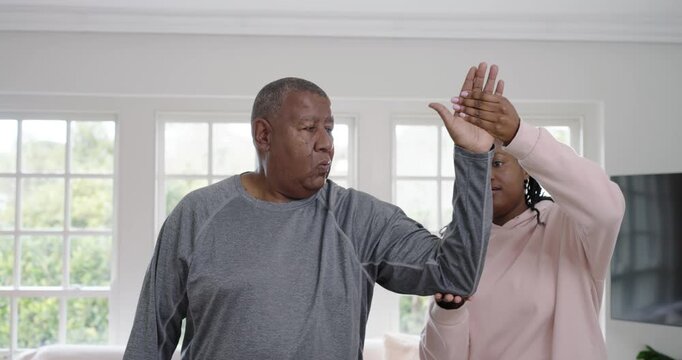 African American caregiver placing hands, guiding Senior man arm mobility exercise in living room