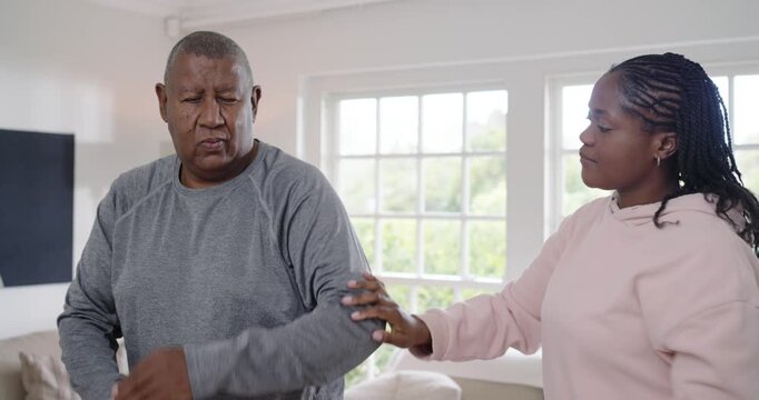 African American daughter moving senior dad's arm after wince at home by window
