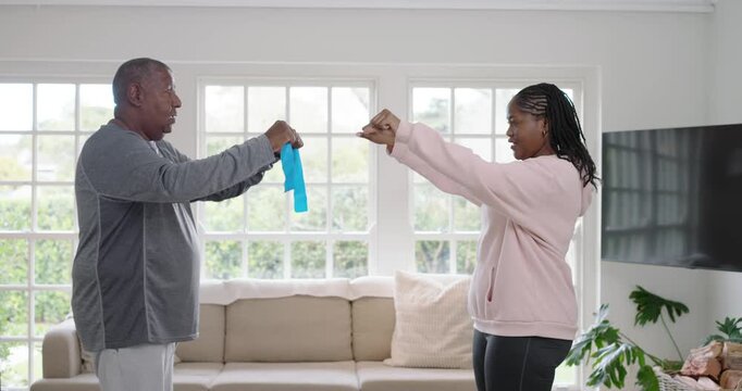 African American man and woman holding blue band, woman pushing, building strength in living room