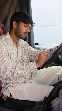 Young indian truck driver writing on clipboard inside cabin