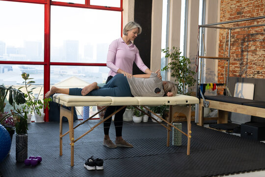 Female practitioner in pink top applying therapy while client lying on massage table in studio