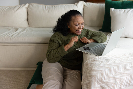 Senior African American woman sitting on living room floor by sofa using laptop with credit card