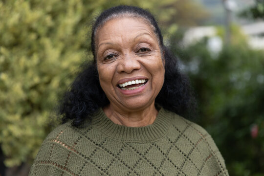 Senior African American woman smiling while posing in garden wearing olive-green knitted sweater