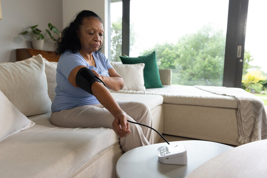 Senior African American woman sitting in living room light-blue shirt checking BP cuff, copy space