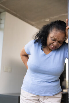 Senior African American woman leaning on doorjamb, holding lower back in doorway
