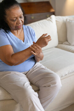 Senior African American woman sitting on pale sofa looking down pressing wrist, bureau, copy space