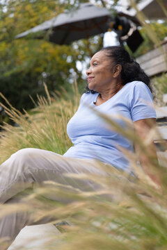 Senior African American woman sitting on stone step in backyard amid tall grasses