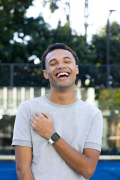 Man laughing while standing at outdoor court wearing light gray T-shirt and square smartwatch