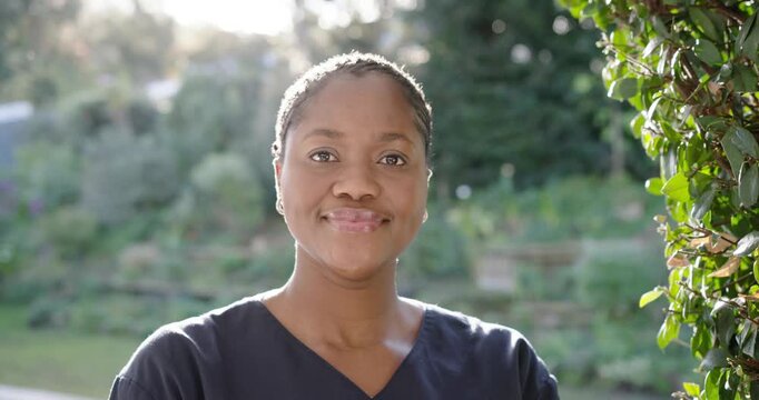 Mid adult African woman smiling as camera pulling back, wearing scrub top and connecting in garden
