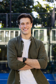 Male standing centered on blue court wearing olive shirt over white tee and dark wristwatch