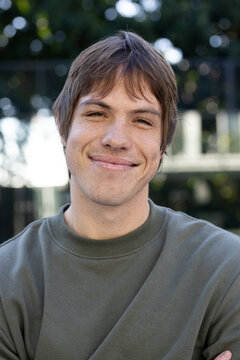 Man with freckles smiling while posing in backyard garden wearing olive-green crewneck sweatshirt