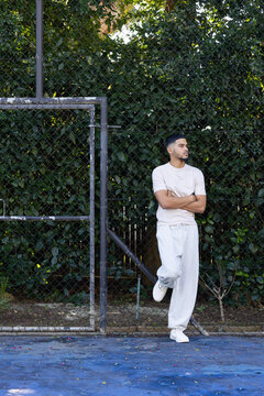 African American man wearing sweats and shoes leaning on chainlink fence at blue court, copy space