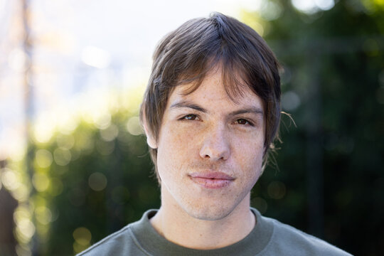 Man with short brown hair and freckles wearing olive-green crewneck sweatshirt, posing in garden