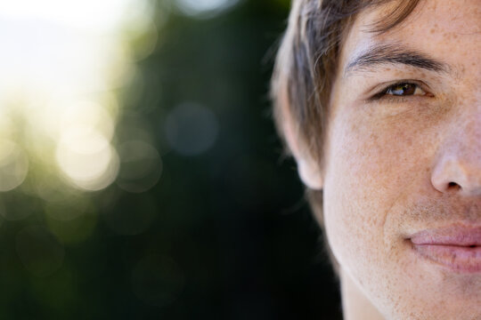 Man showing right half of face with brown eye, freckles, stubble in park bokeh, copy space
