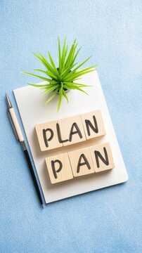 A flat lay view of a blank notebook, cubes with plan, a pen, and a plant on a stylish blue background for business planning concepts