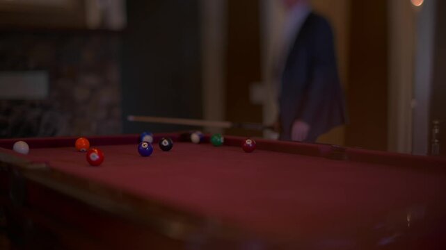 Man in suit plays billiards in a dimly lit room with red felt table