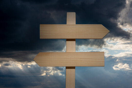 Empty wooden crossroads sign pointing left and right against dramatic dark stormy clouds backdrop, closeup. Conceptual metaphor for difficult decision making strategy and choice