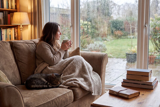 Woman with cat relaxing on sofa during rainy day