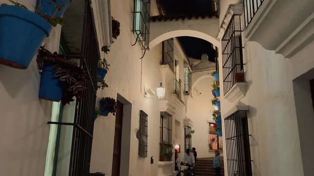 Explore the illuminated streets of Poble Espanyol at night in Barcelona, showcasing traditional Spanish architecture, fortified medieval gate, decorative hanging umbrellas, historic facades,
