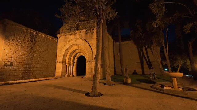 Explore the illuminated streets of Poble Espanyol at night in Barcelona, showcasing traditional Spanish architecture, fortified medieval gate, decorative hanging umbrellas, historic facades,