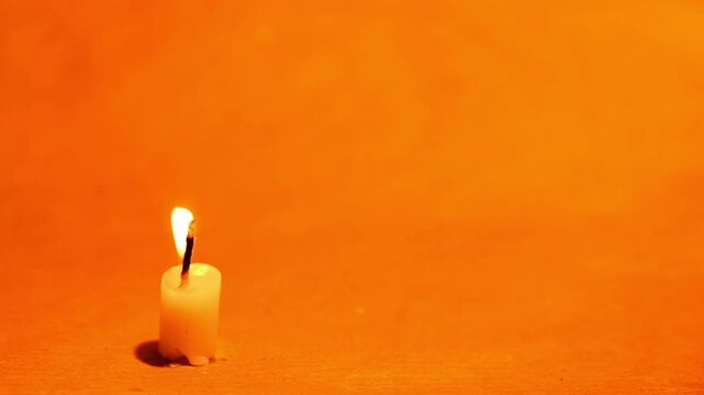 Single white candle burning with a bright flame on an orange background fire light glowing wax wick