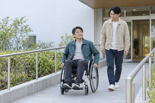 福祉施設のスロープを車椅子で自走する日本人男性と支援員