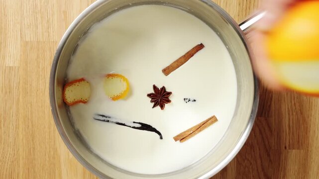 Hands cut orange peel with knife and add it to milk mixture. Zero waste cooking turns citrus skin into natural flavour for custard. This method reduces food waste and adds citrus aroma to dessert.