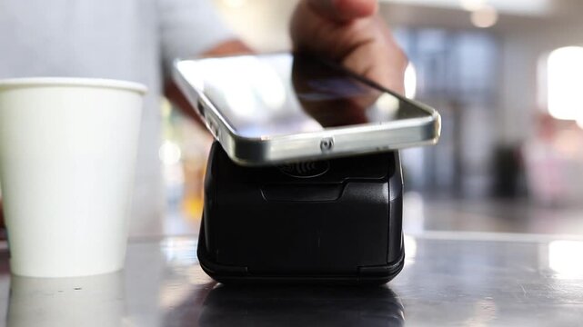 Contactless smartphone payment for coffee using nfc technology on a pos terminal at a cafe counter, showcasing secure transaction